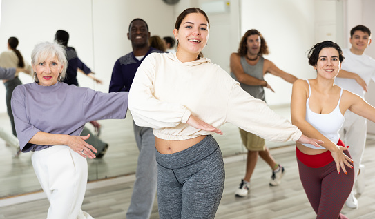 Happy young woman practising modern dance moves with other people in dance studio