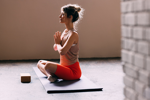 A side view of a serious Caucasian athlete in sports clothes meditating while sitting on her exercise mat.