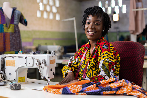 African woman entrepreneur dressmaker  with locs hair working in her fashion design studio with an electric machine.
