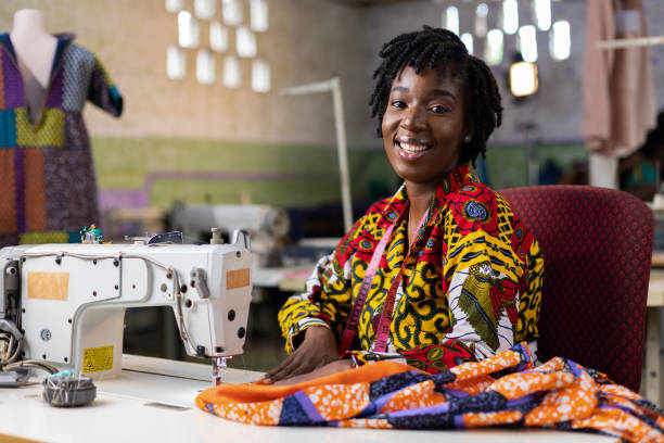 African Dressmaking Entrepreneur African woman entrepreneur dressmaker with locs hair working in her fashion design studio with an electric machine. woman tailor stock pictures, royalty-free photos & images