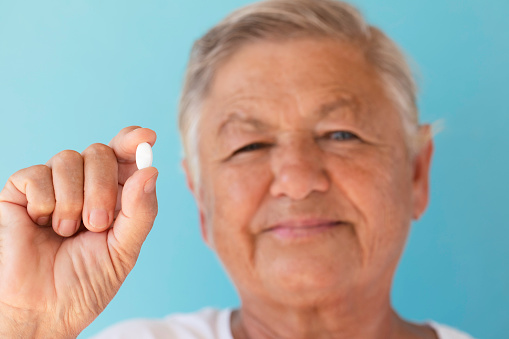 Senior woman holding and showing pill.