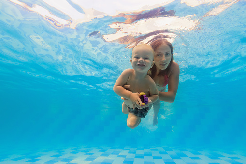Happy family - mother with baby boy swimming and diving underwater with fun in blue pool. Healthy lifestyle, active parents, people water sports activity on summer vacation with child