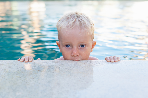 Photo of active baby in swimming pool. Child learn to swim. Healthy family lifestyle, summer children water sport activity and lessons with parents