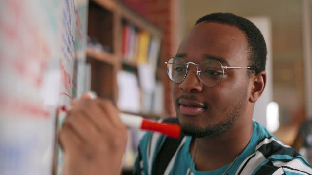 Young black male college student writing notes on a white board