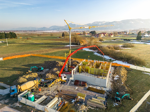 Aerial view of a building construction site in progress with tower crane, pouring concrete, scaffolding, formwork, construction materials, equipment, reinforcing steel bars. Winter time at sunset.