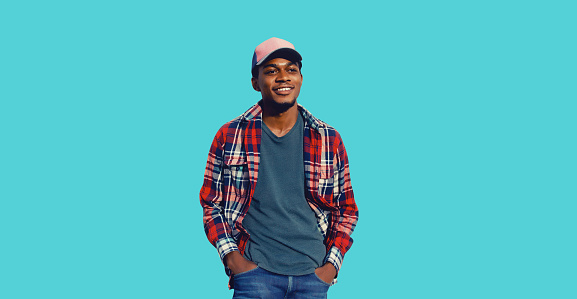 Portrait of stylish smiling young african man posing wearing baseball cap, red plaid shirt isolated on blue background
