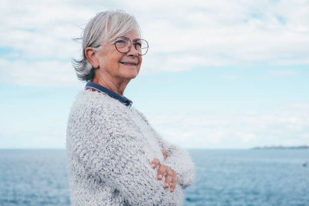 retrato de una mujer mayor pensativa y guapa parada junto al mar mirando hacia otro lado. sonriente anciana de pelo blanco en excursión al aire libre disfrutando de libertad, relax y jubilación - 70 79 años fotografías e imágenes de stock