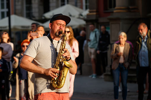 Gdansk, Poland - July 5, 2022: Street musician playing on saxophone. Man saxofonist plays at wind instrument in city for crowd of people