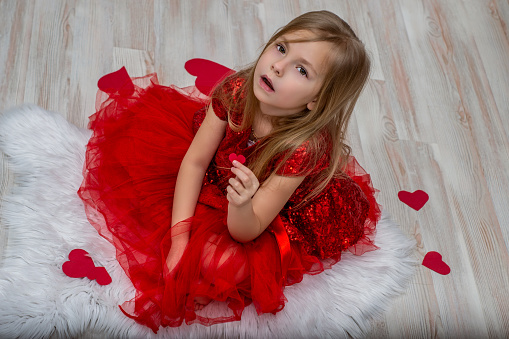 portrait of a beautiful little girl with red heart on a pink background