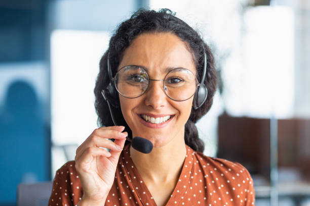 retrato en primer plano de una mujer latinoamericana dentro de una oficina moderna con auriculares para videollamada, mujer sonriendo y mirando a la cámara, línea de ayuda técnica de atención al cliente de oficinista - turkish ethnicity white black contemporary fotografías e imágenes de stock