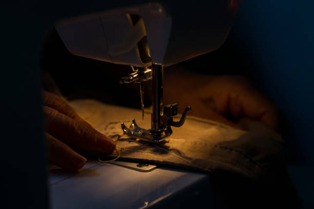 暗い場所でミシンを使う女性 - thread tailor art sewing ストックフォトと画像