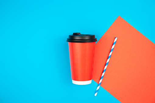 Red paper cup and paper straw for drinks on blue background, flat lay, ecology concept, copy space.