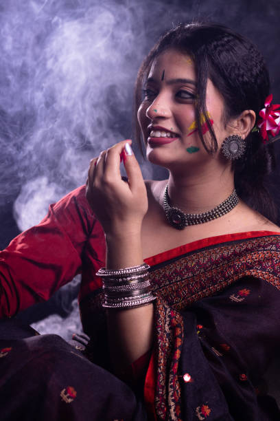 Young Indian girl woman in ethnic attire saree playing with organic dry color powder gulal abeer smiling celebrating Holi festival of colors with smoke in the background stock photo