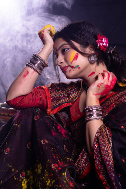 Young Indian girl woman in saree with organic dry color powder gulal abeer on face pose for photo celebrating Holi festival of colors with smoke fragrance in the background stock photo
