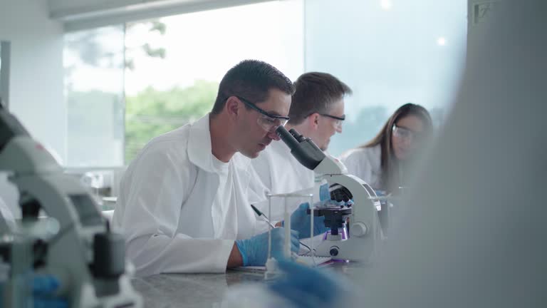 Adult students analyzing object under microscope in laboratory