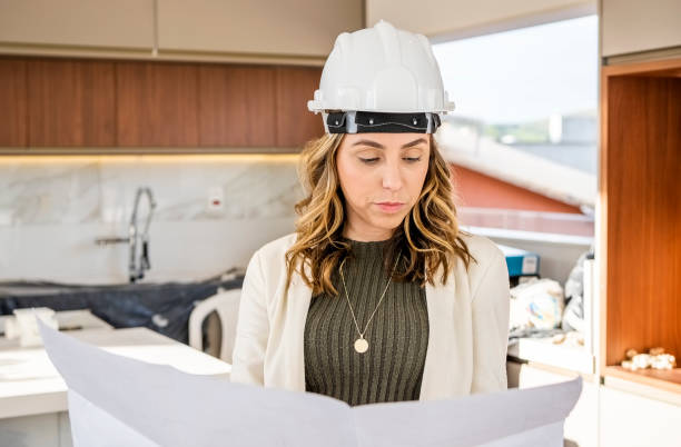 istock Young woman architect wearing hardhat reviewing a renovation plan at construction site 1465654878