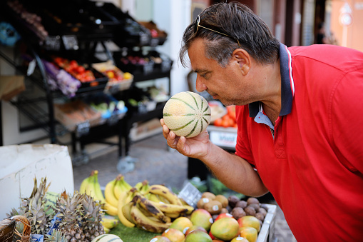 Overweight Man chef smelling vegetables on local organic market. Choose food for his Mediterranean cooking in European trip