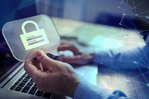 Closeup of businessman working on a laptop while holding on one hand a message bubble showing a lock. Focus is on the lock symbol meaning online information security