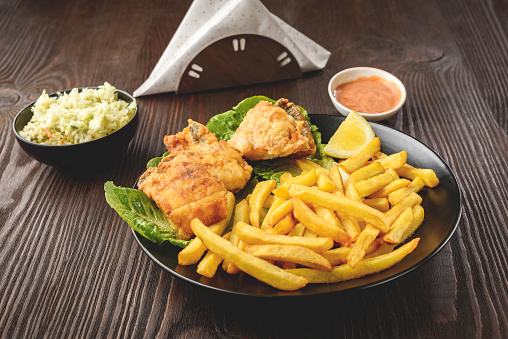 fish and chips on a black plate, served with salad and sauce