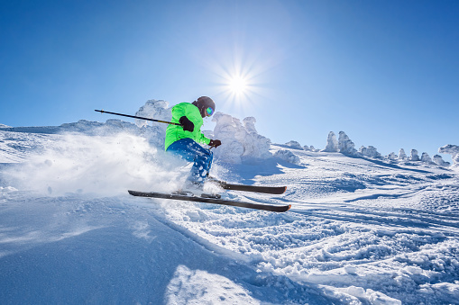 Skier skiing downhill in high mountains during sunny day.