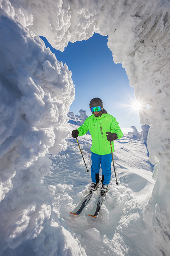 Skier posing in front of ice cave in high mountains against sunset.