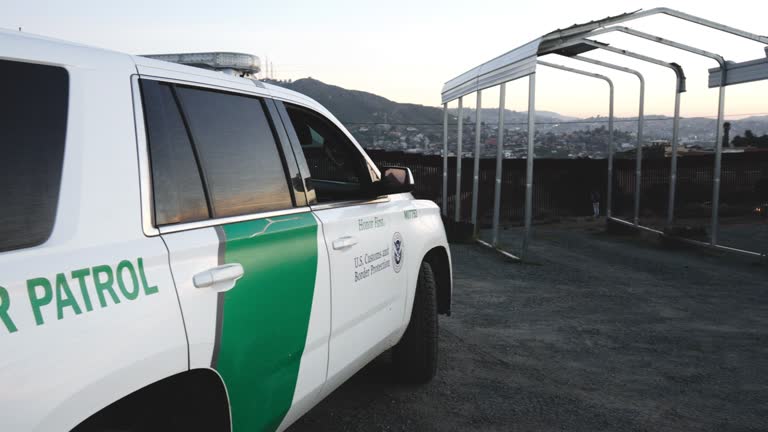 U.S. Border Patrol Official Vehicle Parked Near the International Border Barrier Wall Between the United States and Mexico in Tecate California at Dusk With Pretty Cloudscape