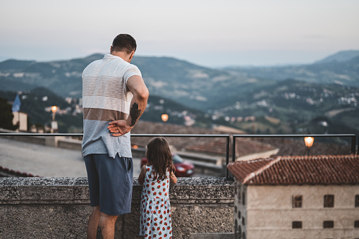father and daughter on a rock overlooking the city. , back view. dad with child in vacation sighnseeing