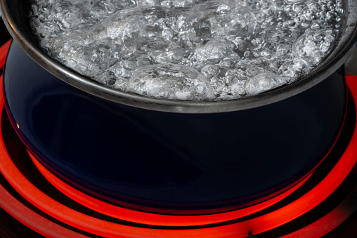 Horizontal shot of a blue pot on a stove top on a red hot burner holding boiling water.  Only part of the pot shows.