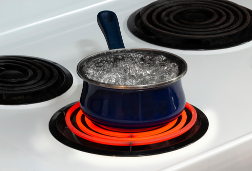 Horizontal shot of a blue pot on a stove top on a red hot burner holding boiling water.  Copy space.