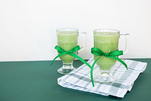 Two healthy green smoothies sitting on folded plaid towel on green and white background.