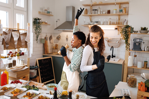 Two young female chefs dancing in their small domestic food store