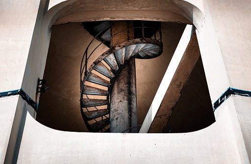 View of old metal spiral staircase inside columnar structures old water tower made of cement. Dark tone, Selective focus.