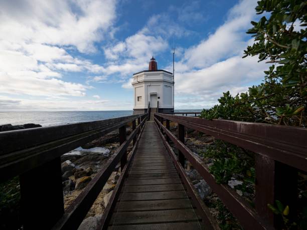 istock Wooden pathway boardwalk leading to historical white Stirling Point lighthouse navigation building in Bluff New Zealand 1465700580