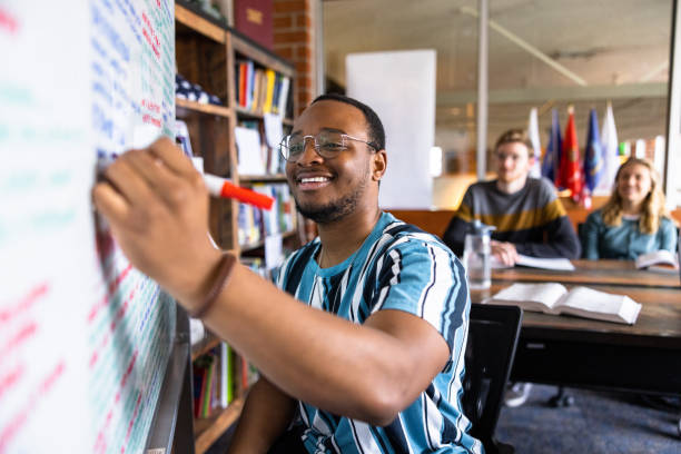 Young black male college student writing notes on a white board stock photo