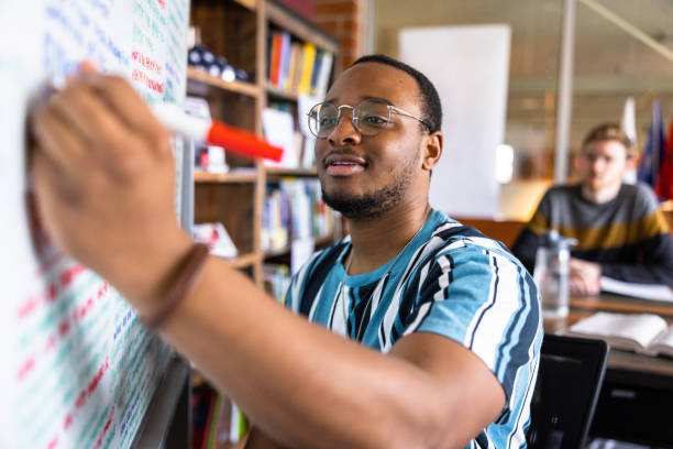 istock Young black male college student writing notes on a white board 1465708338