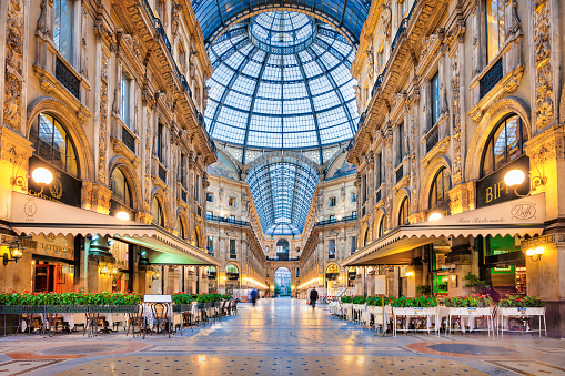 People walk inside Galleria Vittorio Emanuele II Shopping Arcade in Milan, Lombardy, Italy at dawn.