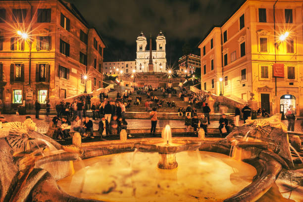 People enjoy Piazza di Spagna, with the Spanish Steps (Scalinata) in the background, in downtown Rome, Italy in the evening.
