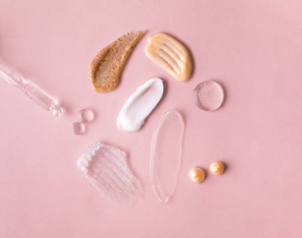 Swatches from various cosmetic products, drops of lotion, smears of creams, gels and scrubs on pink background stock photo