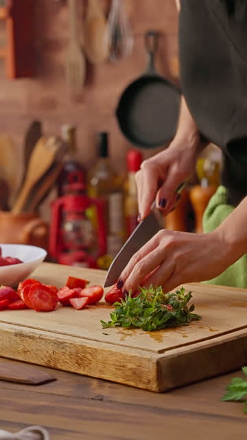 Close-up of woman hands slicing strawberries on a cutting board in a bowl to prepare marmalade preserves.