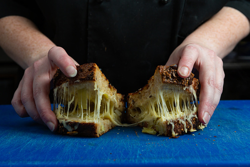 A chef's hands are seen pulling apart a freshly made toasted sandwich, or toastie. Strings of hot cheese are seen forming.