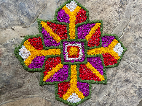 Horizontal high angle closeup photo of bright colourful flowers and leaves arranged in a mandala pattern on a paved stone floor. Bali, Indonesia.