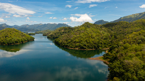 Aerial drone of river among mountains and hills with a forest against the sky and clouds. Randenigala reservoir, Sri Lanka.