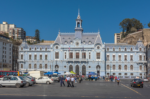 Bogota, Colombia - July 01, 2016: People sit on the steps of the Cathedral on Plaza Bolivar to take a break and watch the world go by. The small building to the right, with the terracotta roof tiles is the Casa del Florero, the flashpoint from where the Freedom Movement for 5 South American Countries commenced. To the left of the image, many local Colombians go about their day to day life. The Eastern Mountains can be seen in the far background. The sky is overcast; it is drizzling a bit causing some people to open their umbrellas. The altutude at street level is about 8,500 feet above sea level and most people wear warm clothes. Photo shot in the afternoon sunlight on an overcast day; horizontal format. Copy space.