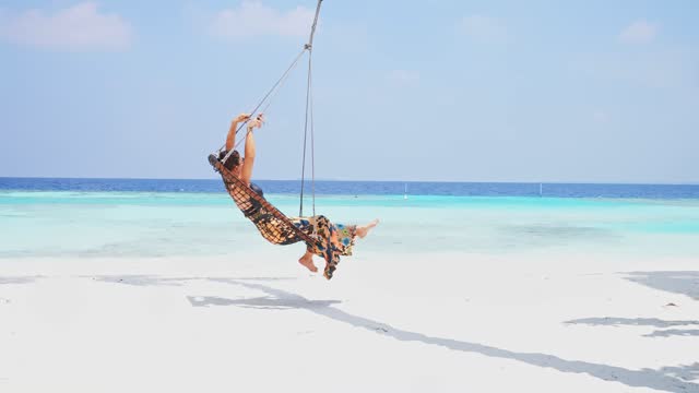 Woman relaxing on the swing in tropical ocean beach