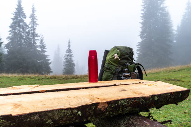 Travel thermos for hot drinks and backpack. Hiking with a thermos and a backpack. Camping. Hiking with a big backpack. Table in the forest.
