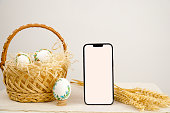 Easter holiday phone with white background basket eggs with embroidered pattern ribbon embroidery on eggshells wheat spikelets on table place for dough close-up basket to church white screen