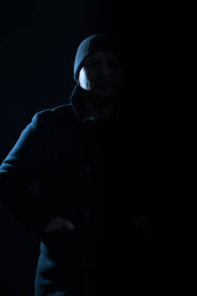 istock Man with coat and hat hiding in shadow and silhouette illuminate with light 1465750011