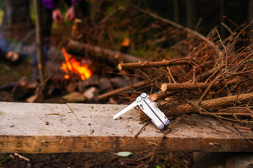 Folding pocket saw. A saw, branches and a fire. Breeding fire in nature. Cut branches for the fire. Front view.