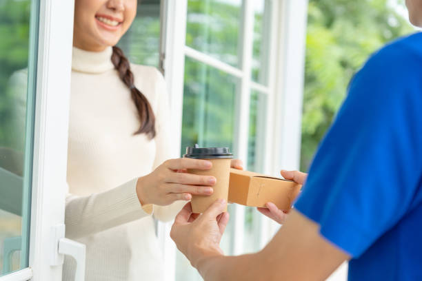 istock Happy smiling woman receives boxes parcel from courier in front house. Delivery man send deliver express. online shopping, paper containers, takeaway, postman, delivery service,  packages 1465757575