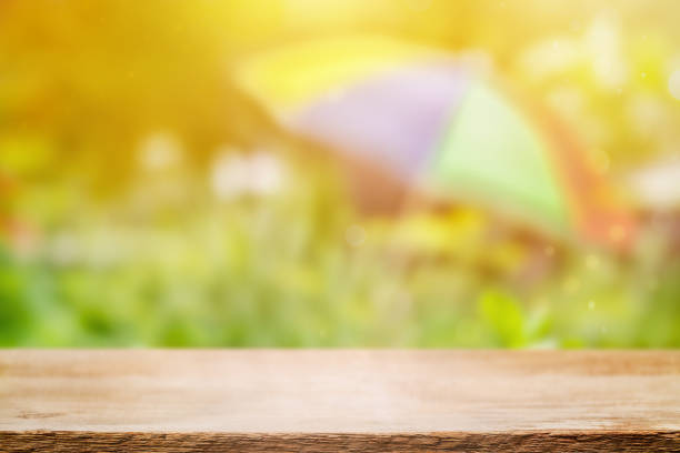 istock Empty wooden table on a summer background with a multicolored umbrella - product placement 1465760275
